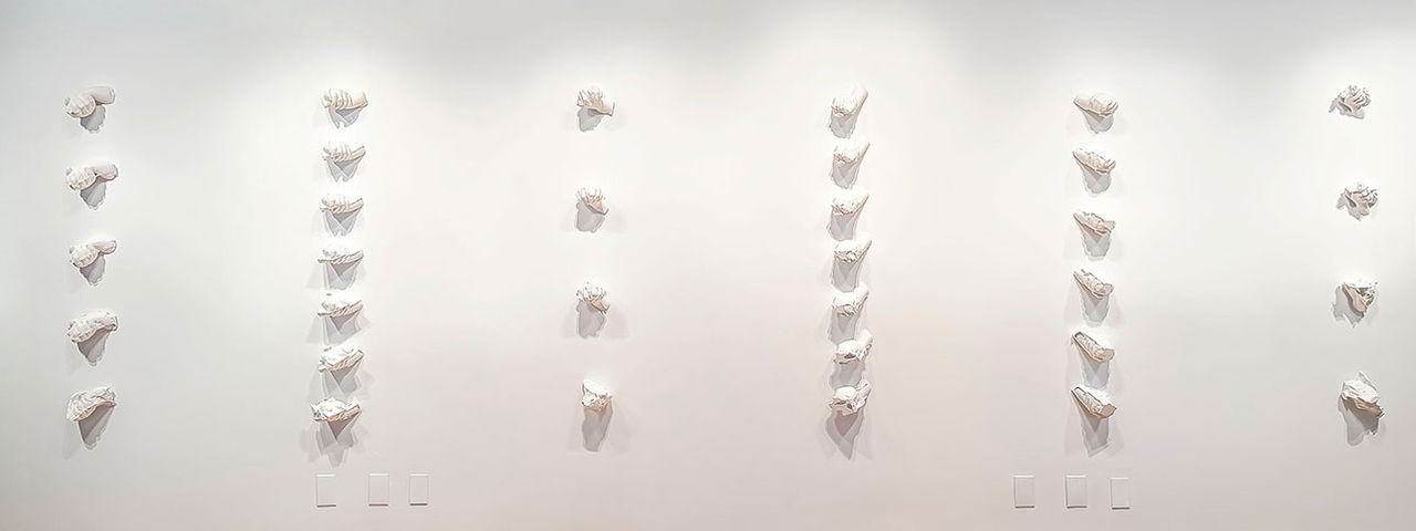 White plaster hand fragments mounted in vertical rows across a gallery wall