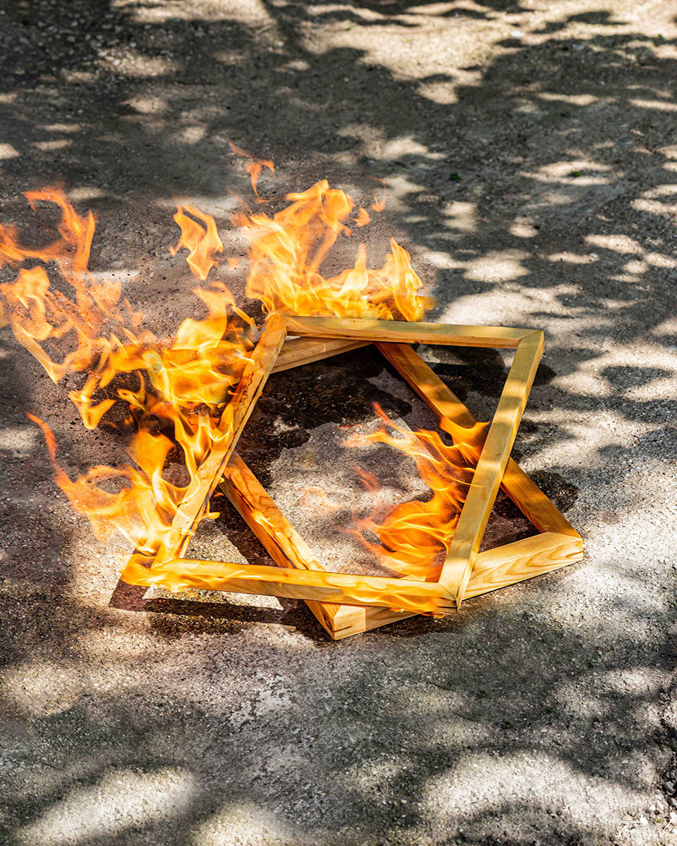 Color photograph of burning canvases stretchers on pavement titled "the need to rebuild (restructure and start again)" by Jesse Ly, 2022; photograph in UC DAAP Galleries' Reed Gallery Exhibit Long Exposure